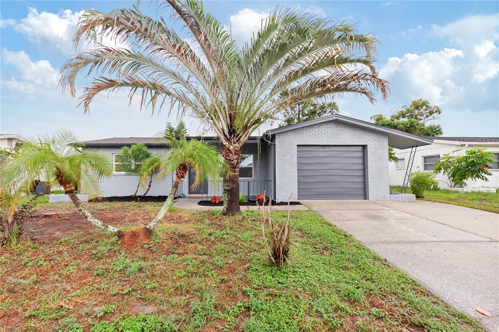 A single-story gray brick house features a garage, a driveway, and several palm trees — 9324 WHITMAN LANE, PORT RICHEY, FL