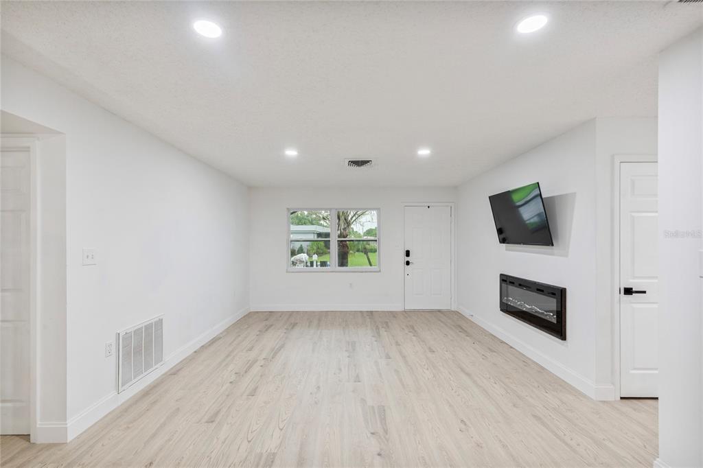 A living room features light wood-look flooring, white walls, recessed lighting, a fireplace, and television — 9324 WHITMAN LANE, PORT RICHEY, FL