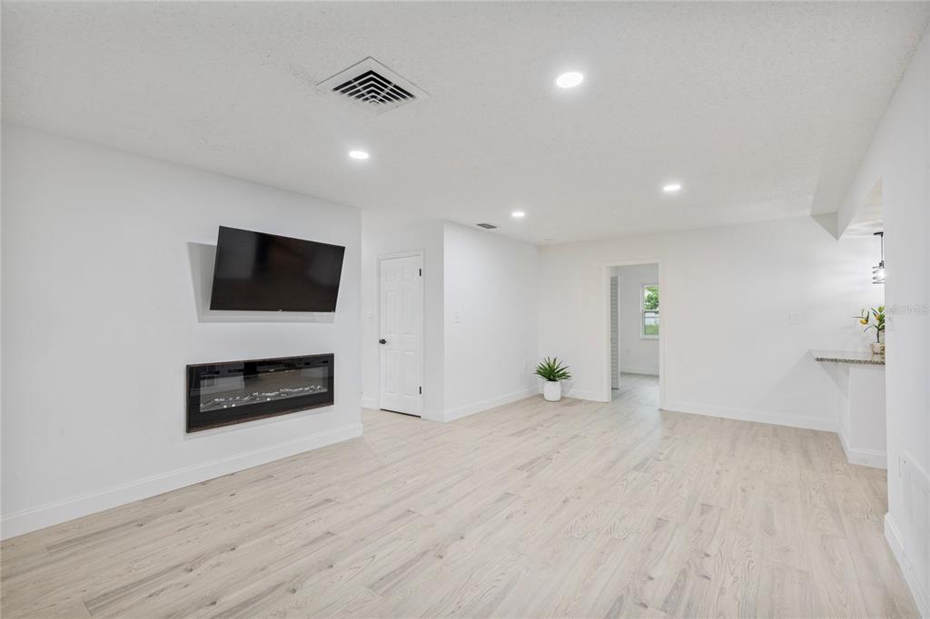 A bright living room features light wood flooring, a wall-mounted television, and a built-in fireplace — 9324 WHITMAN LANE, PORT RICHEY, FL