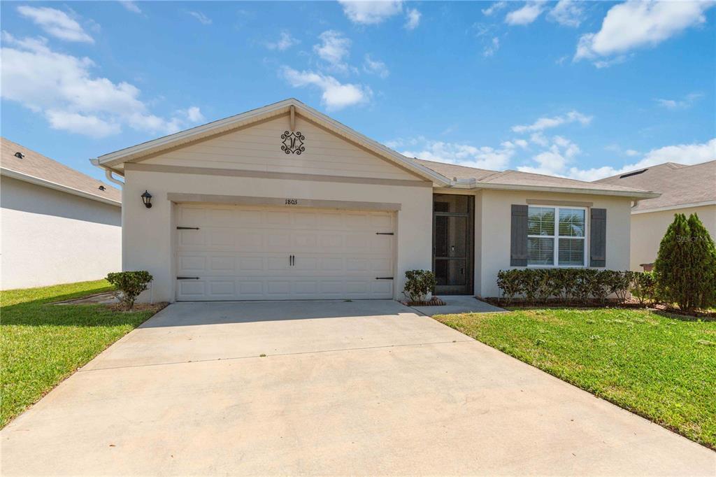 A single-story house with a beige stucco exterior, a two-car garage, and a front lawn — 1803 RAIN LILY PLACE, ST CLOUD, FL