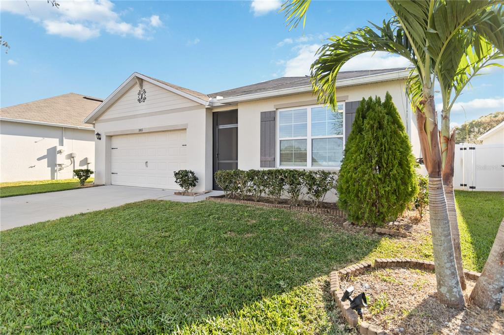 A single-story house with a white stucco exterior, a two-car garage, and a palm tree — 1803 RAIN LILY PLACE, ST CLOUD, FL