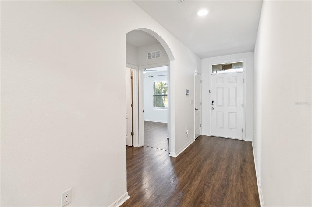 A bright entryway features dark wood-look flooring, white walls, and an arched doorway — 1803 RAIN LILY PLACE, ST CLOUD, FL