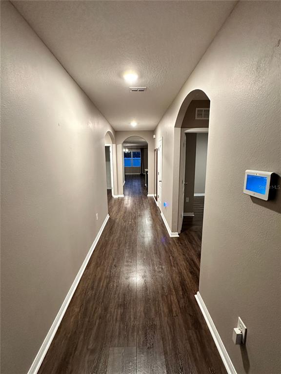 A long hallway with dark wood-look flooring leads to an arched doorway and a window — 1803 RAIN LILY PLACE, ST CLOUD, FL