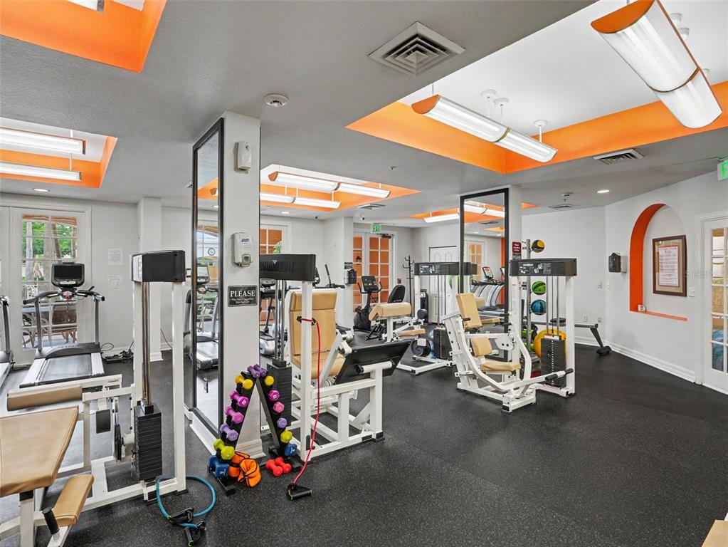 A gym with various exercise machines, a dumbbell rack, and orange-accented recessed ceiling lighting — 501 MIRASOL CIRCLE UNIT 313, CELEBRATION, FL
