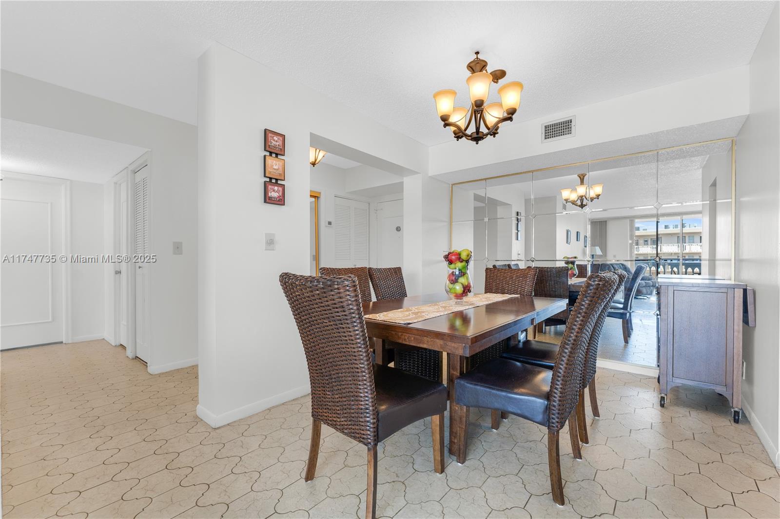 A dining room features a wooden table with wicker chairs, a chandelier, and mirrored walls — 401 NE 14th Ave # 603, Hallandale Beach FL 33009, HALLANDALE BEACH, FL