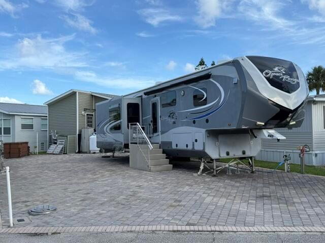 A gray Open Range fifth-wheel RV is parked on a paved lot next to a house — 883 Nettles Boulevard, Jensen Beach FL 34957, JENSEN BEACH, FL