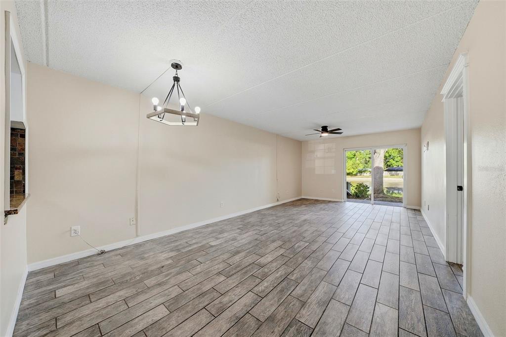 An empty living room features wood-look tile flooring, a chandelier, and a sliding glass door — 3821 N OAK DRIVE UNIT J21, TAMPA, FL