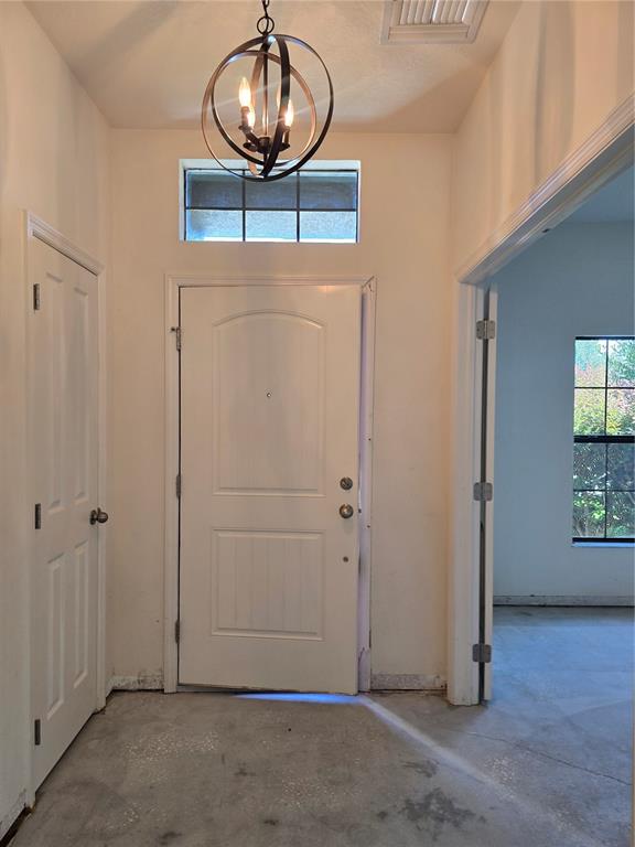 An entryway features a white front door, a spherical chandelier, and unfinished concrete flooring — 14282 SALTBY PLACE, SPRING HILL, FL