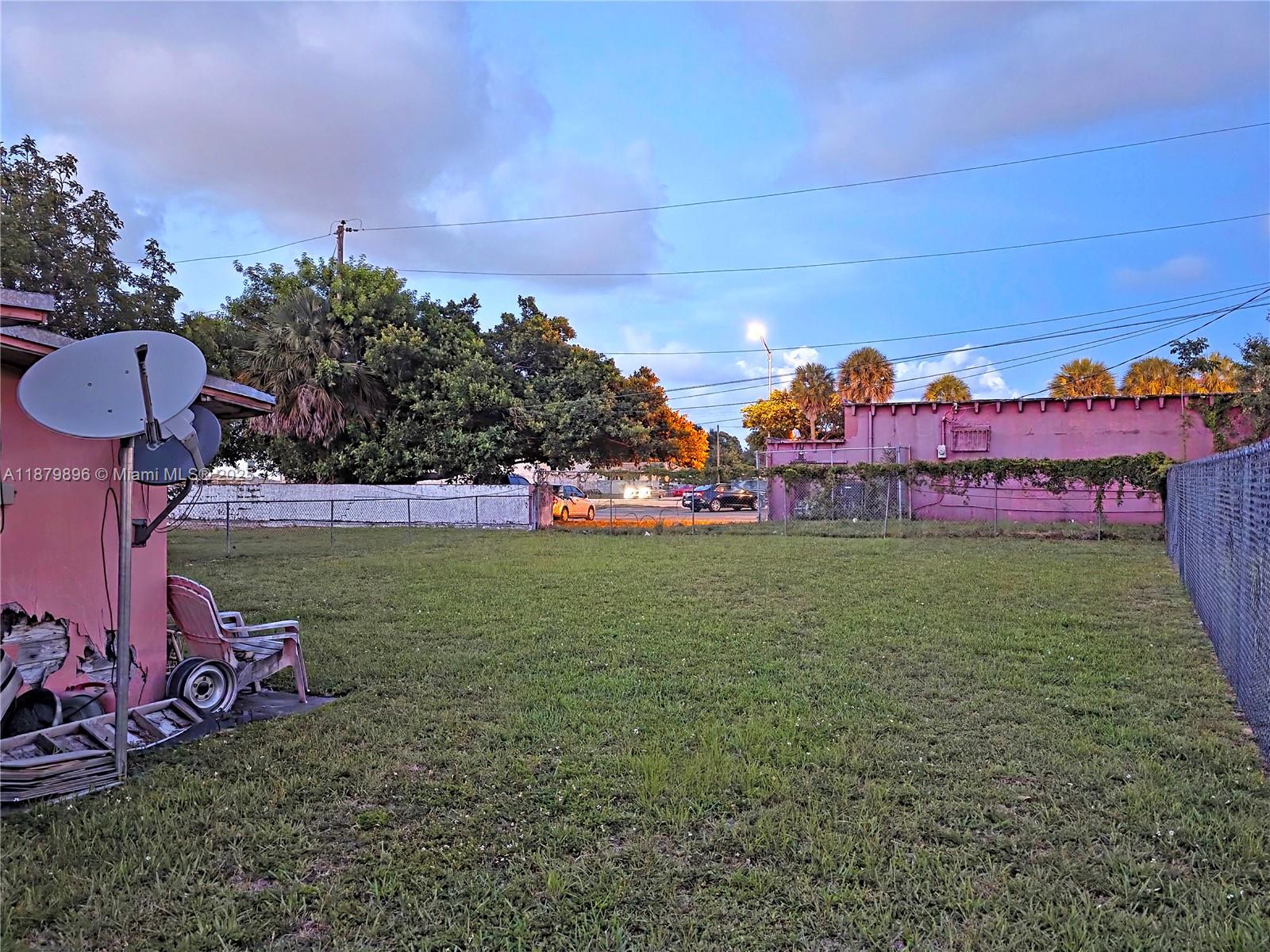 A grassy backyard features a satellite dish, a pink wall, and a chain-link fence — 6233 NW 22nd Ct, Miami FL 33147, MIAMI, FL