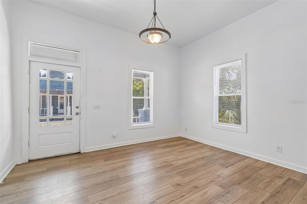 An empty room features white walls, wood-look flooring, a hanging light fixture, and two windows — 2601 N 19TH STREET, TAMPA, FL