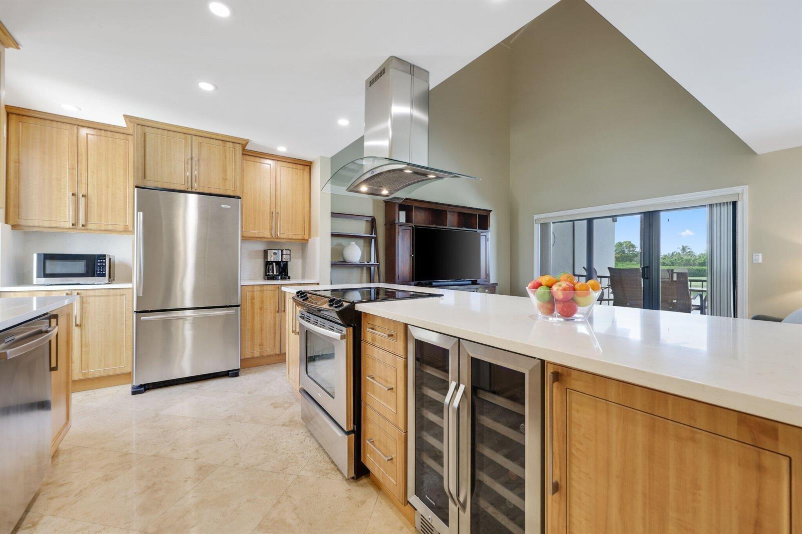 A kitchen features light wood cabinets, stainless steel appliances, a center island, and vaulted ceilings — 800 Greensward Court # I, Delray Beach FL 33445, DELRAY BEACH, FL