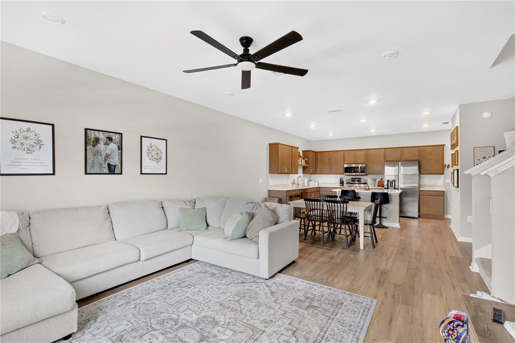 An open-concept living room and kitchen featuring light wood flooring and a large sectional sofa — 5836 FRESHWATER CANYON DRIVE, ST CLOUD, FL