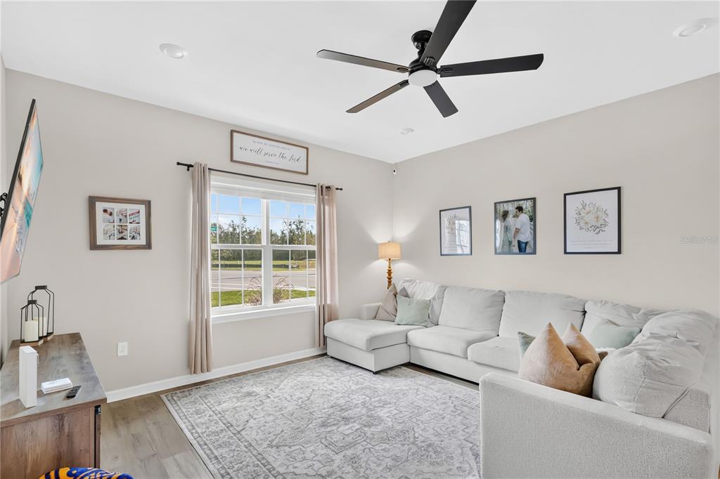 A living room features a sectional sofa, a ceiling fan, and a window with curtains — 5836 FRESHWATER CANYON DRIVE, ST CLOUD, FL