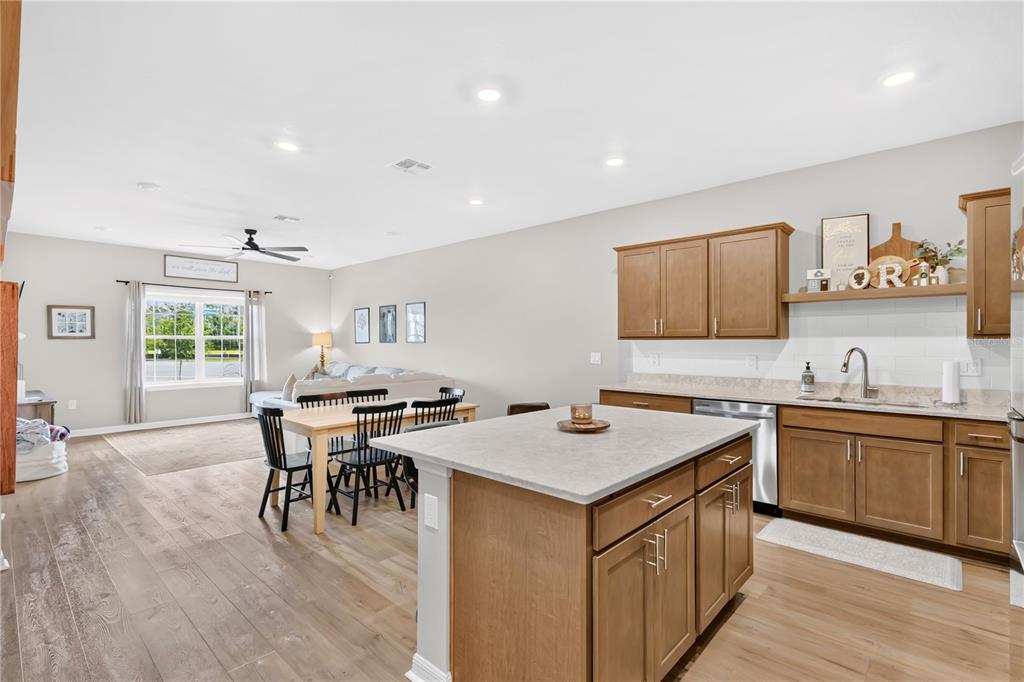 An open-concept kitchen with wood cabinets and a central island overlooks a dining and living area — 5836 FRESHWATER CANYON DRIVE, ST CLOUD, FL