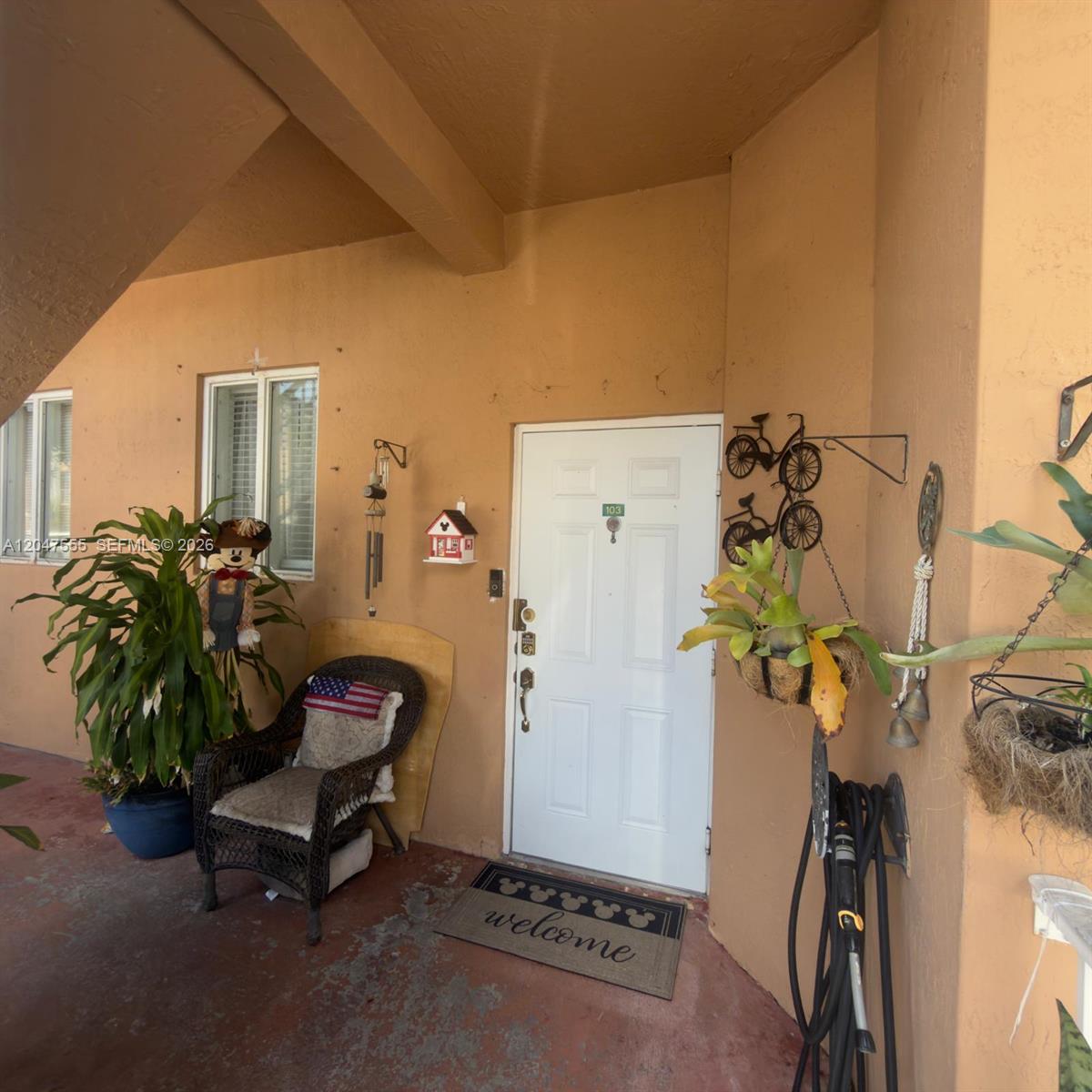 A covered entryway features a white front door, a wicker chair, and potted plants — 17820 NW 73rd Ave # 1, Hialeah FL 33015, HIALEAH, FL