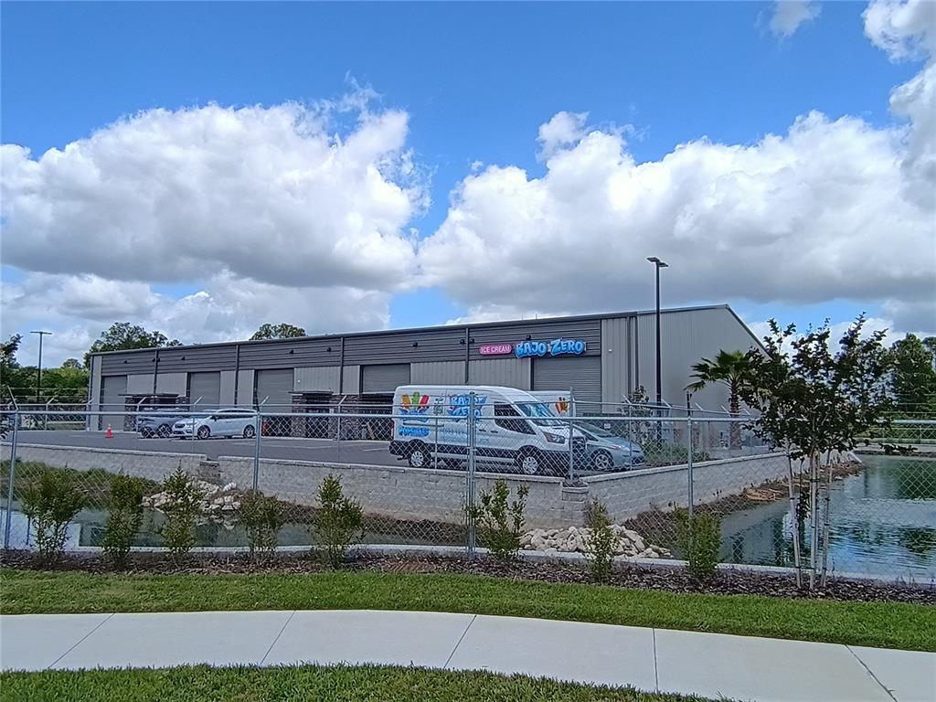 A commercial warehouse building with a fenced parking lot and a small pond in front — 1800 CORPORATE CENTER LANE, PLANT CITY, FL