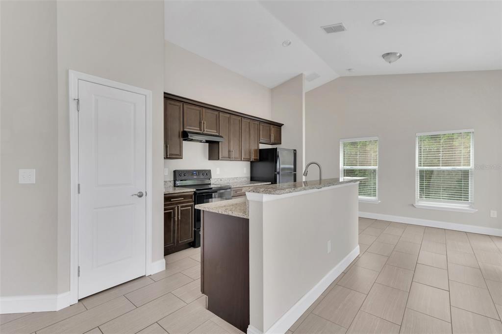 A kitchen with dark wood cabinets, granite countertops, and tile flooring in an open floor plan — 1206 BEECHDALE COURT, DELTONA, FL