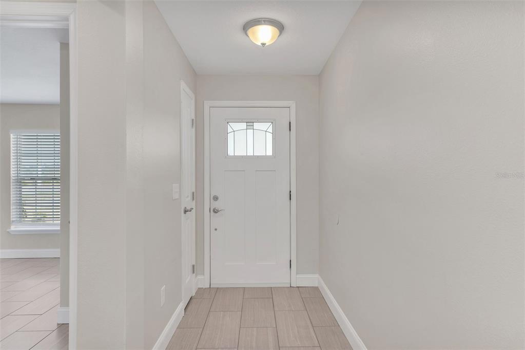 An entryway features a white front door, light-colored walls, and tile flooring — 1206 BEECHDALE COURT, DELTONA, FL