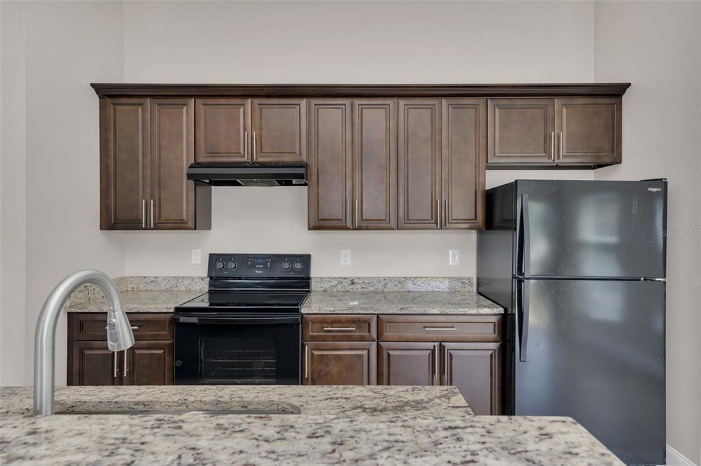 A kitchen features dark wood cabinets, granite countertops, and black appliances — 1206 BEECHDALE COURT, DELTONA, FL