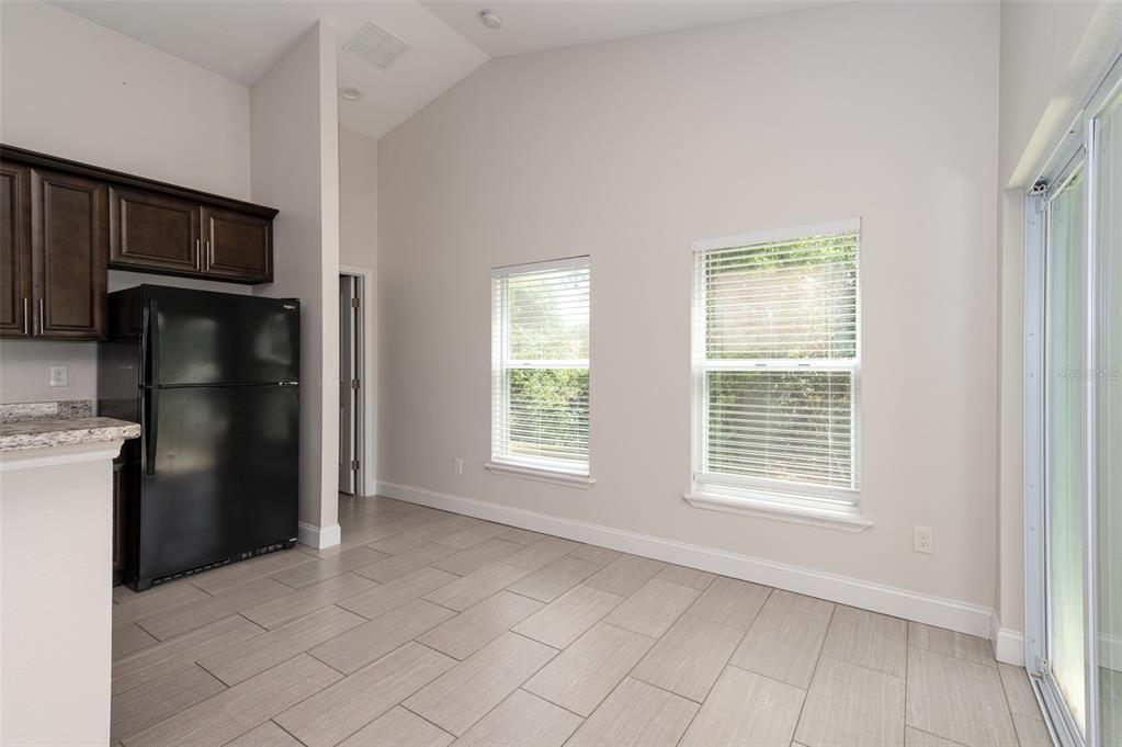 A kitchen and dining area with tile flooring, a black refrigerator, and two windows — 1206 BEECHDALE COURT, DELTONA, FL