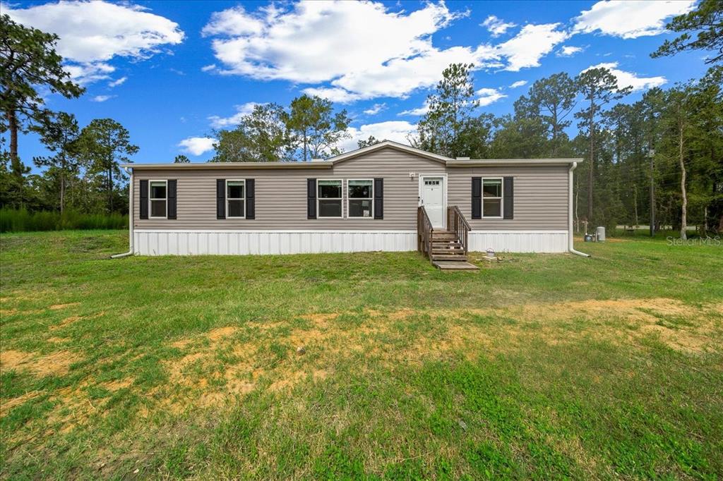 A single-story manufactured home with gray siding and a small wooden front porch — 8500 E HIGHWAY 318, CITRA, FL