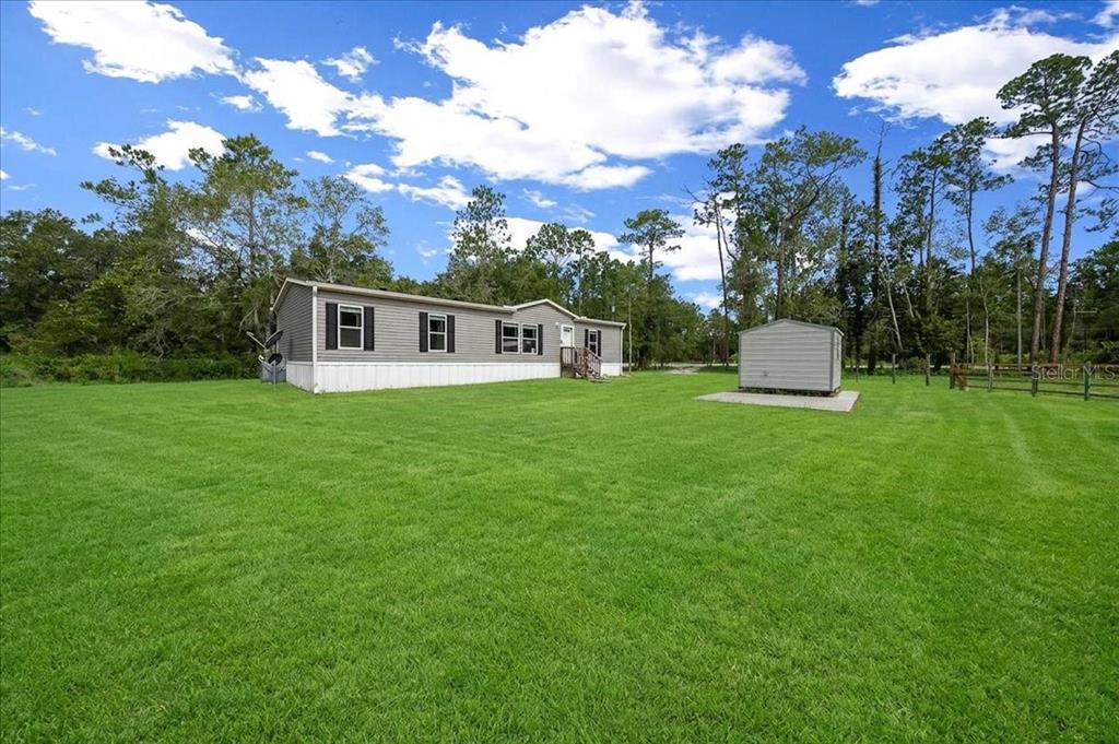 A gray manufactured home sits on a large, grassy lot with a detached storage shed — 8500 E HIGHWAY 318, CITRA, FL