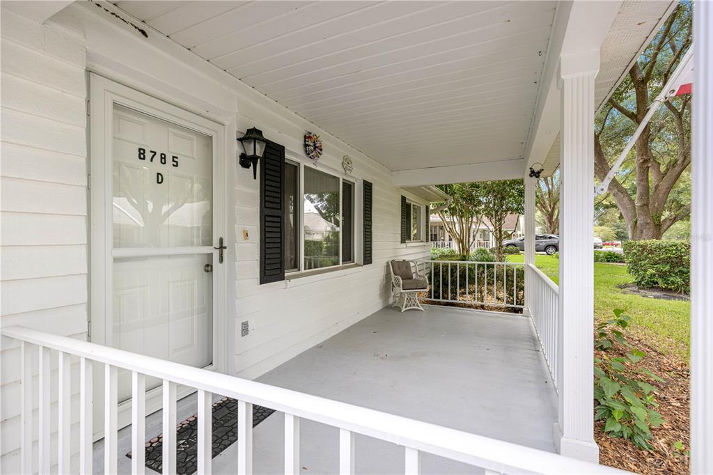 A covered front porch features white siding, a white railing, and a glass storm door — 8785 SW 91ST STREET UNIT D, OCALA, FL