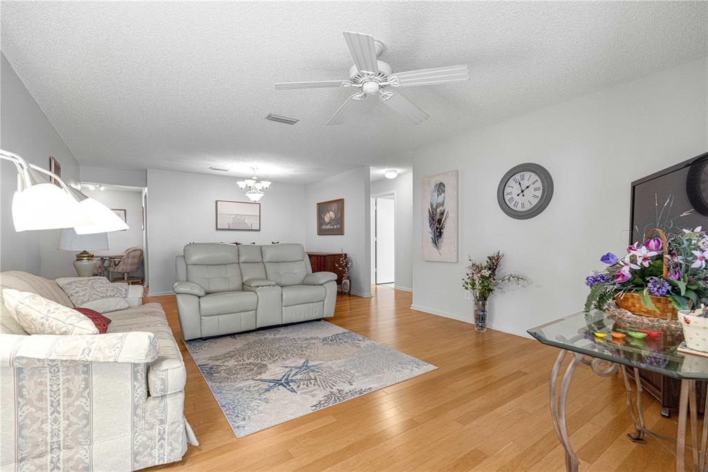 A living room features light-colored furniture, a patterned area rug, and hardwood flooring — 8785 SW 91ST STREET UNIT D, OCALA, FL