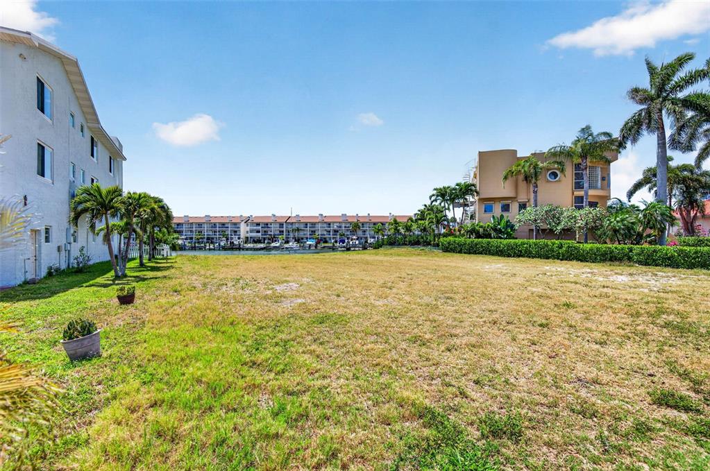 A grassy vacant lot sits between a white building and a tan multi-story structure — 1 1ST AVENUE S, TIERRA VERDE, FL