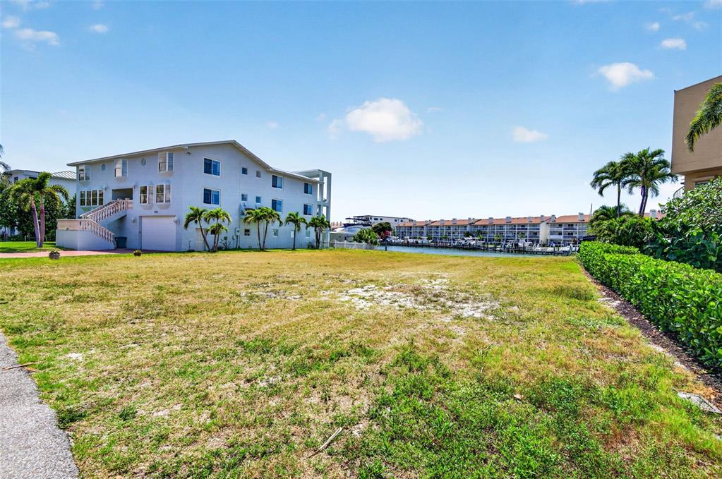 A vacant grassy lot sits next to a multi-story building near a canal with boats — 1 1ST AVENUE S, TIERRA VERDE, FL