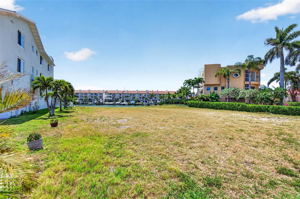 A grassy vacant lot sits between two multi-story residential buildings near a canal — 1 1ST AVENUE S, TIERRA VERDE, FL