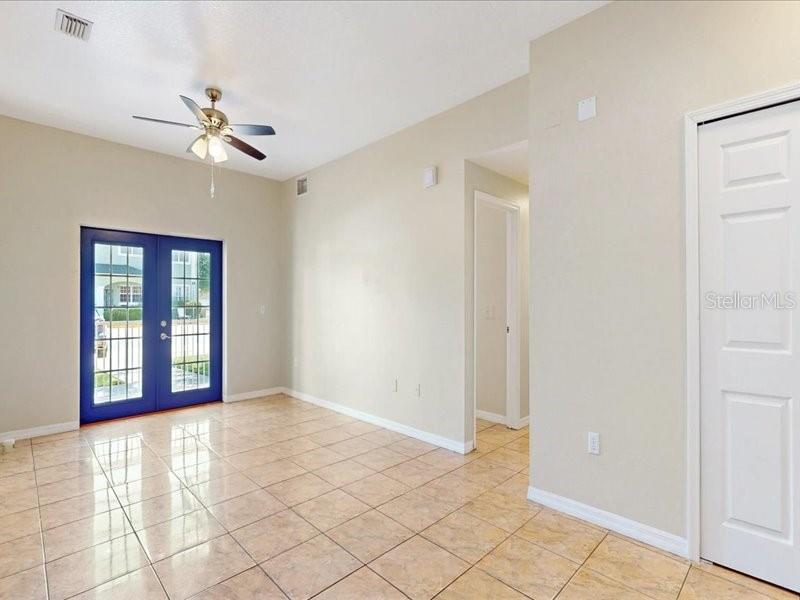A room with beige walls, tiled floors, a ceiling fan, and blue French doors — 206 MAJORS LANE UNIT B, KISSIMMEE, FL