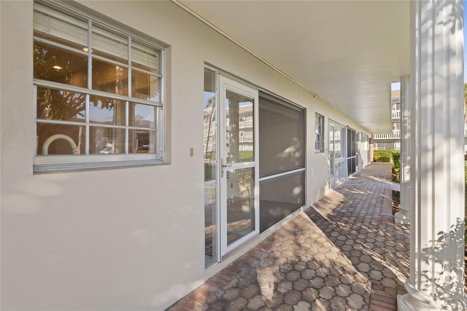 A paved walkway runs along the exterior wall of a building with windows and screen doors — 1965 SE 5th Court # 104, Pompano Beach FL 33060, POMPANO BEACH, FL