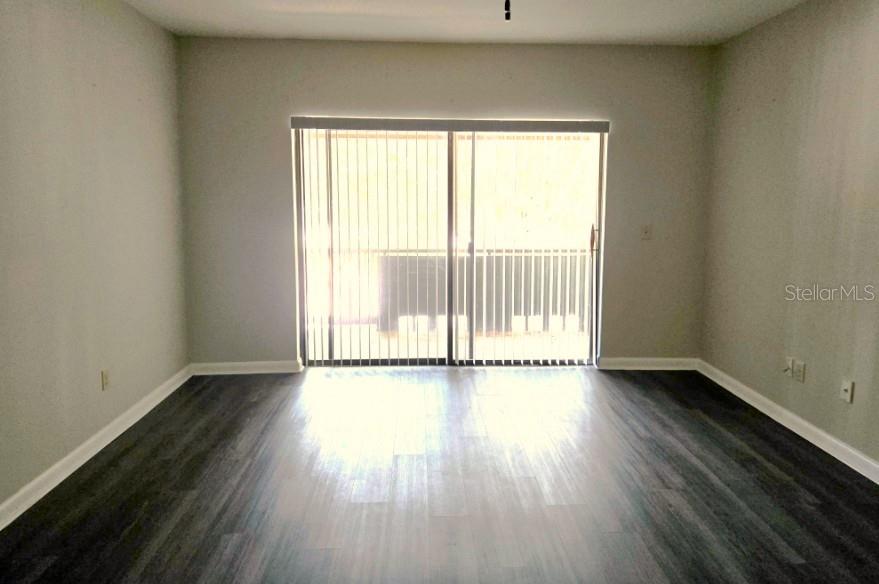 An empty room with gray walls, dark wood-look flooring, and a sliding glass door — 3545 E FORT KING STREET UNIT 257, OCALA, FL
