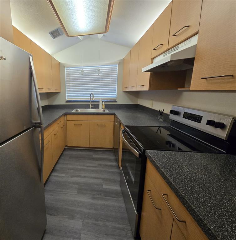 A galley kitchen features light wood cabinets, dark countertops, stainless steel appliances, and gray flooring — 3545 E FORT KING STREET UNIT 257, OCALA, FL