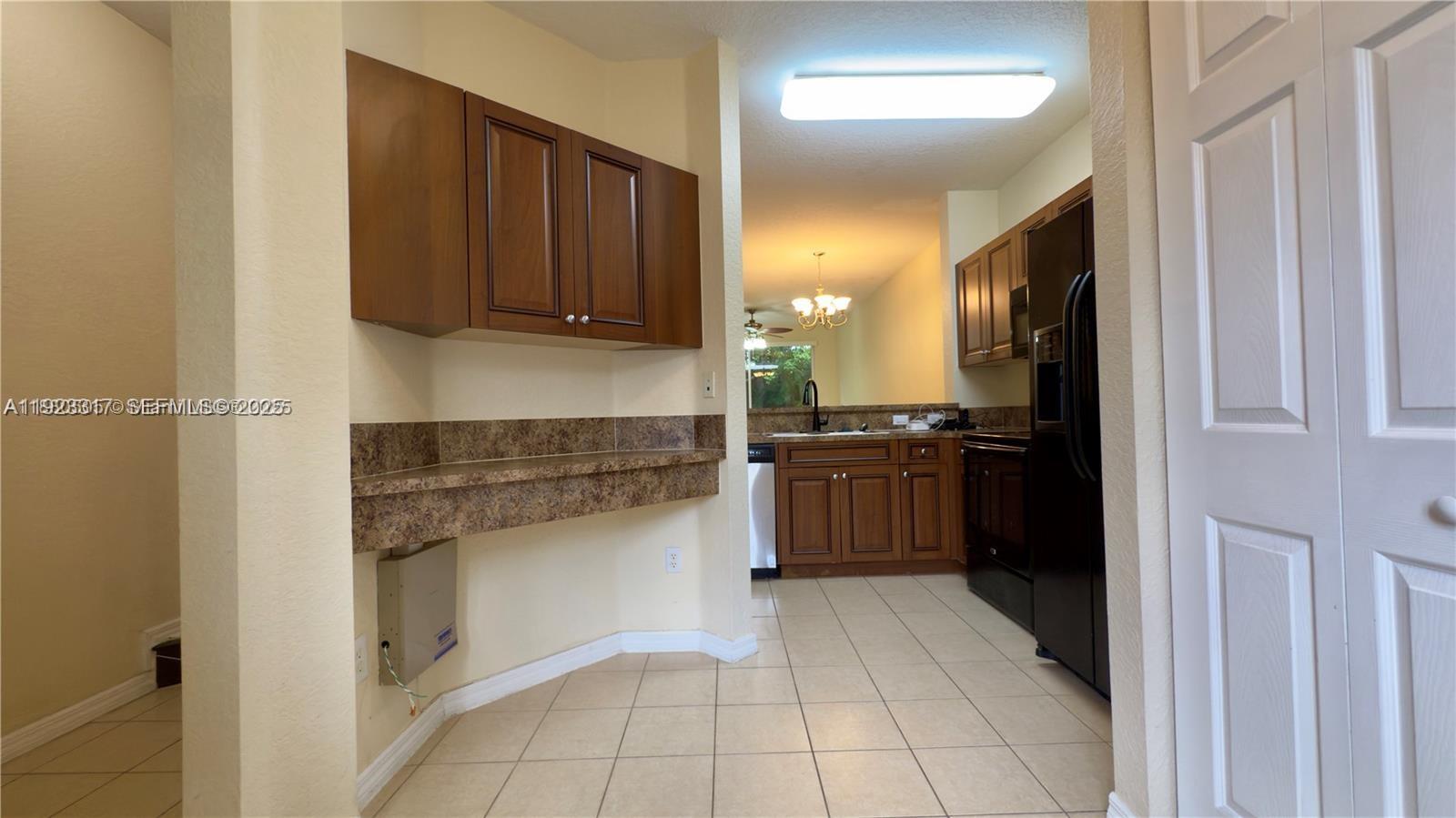 A kitchen features wood cabinets, dark countertops, and tile flooring — 1918 Alamanda Way, Riviera Beach FL 33404, RIVIERA BEACH, FL