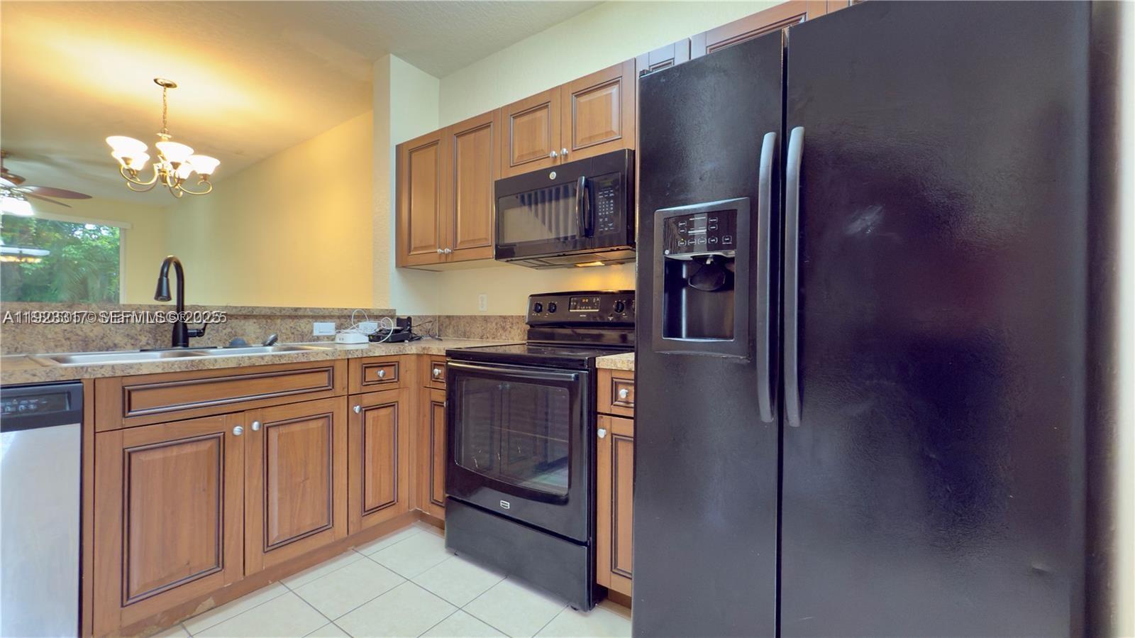 A kitchen features wood cabinets, black appliances, and a granite countertop with a sink — 1918 Alamanda Way, Riviera Beach FL 33404, RIVIERA BEACH, FL