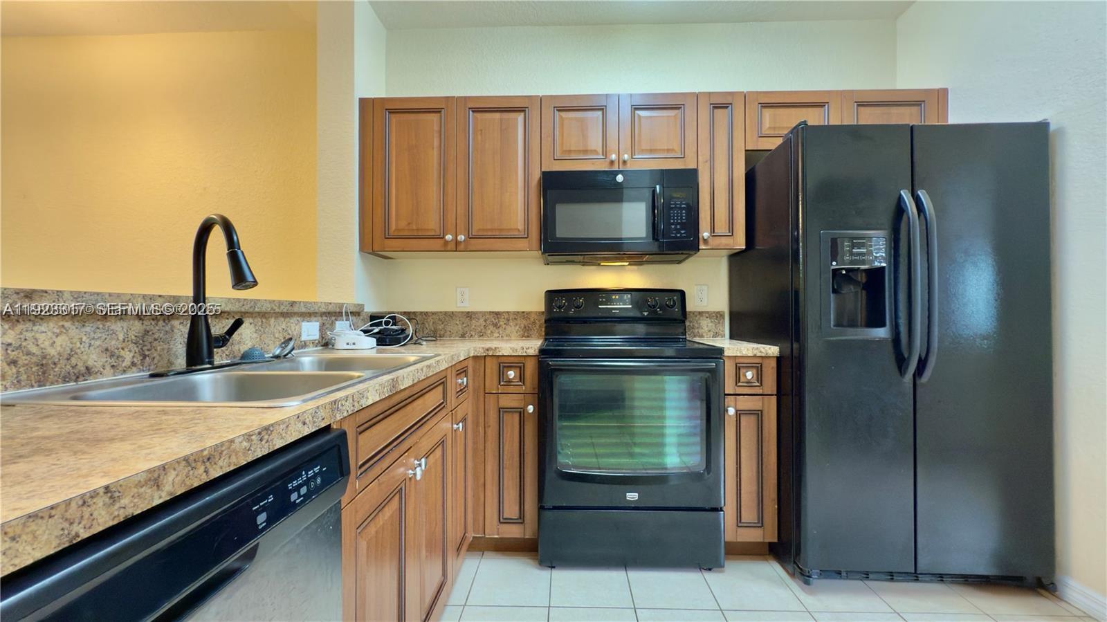 A kitchen features wood cabinets, black appliances, a double sink, and speckled laminate countertops — 1918 Alamanda Way, Riviera Beach FL 33404, RIVIERA BEACH, FL