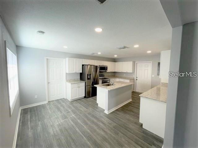 A kitchen features white cabinets, stainless steel appliances, a center island, and gray wood flooring — 705 HARLAND COURT, KISSIMMEE, FL