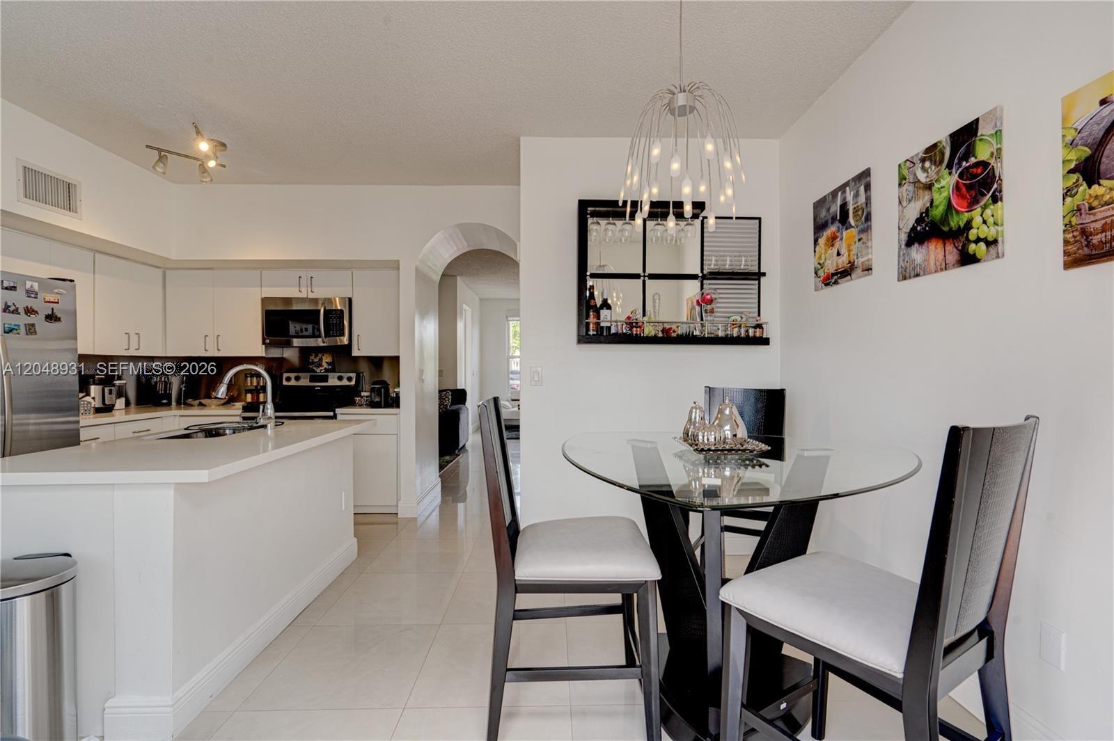 A kitchen with white cabinets and a dining area featuring a glass table and chairs — 8535 SW 152nd Ave # 204, Miami FL 33193, MIAMI, FL