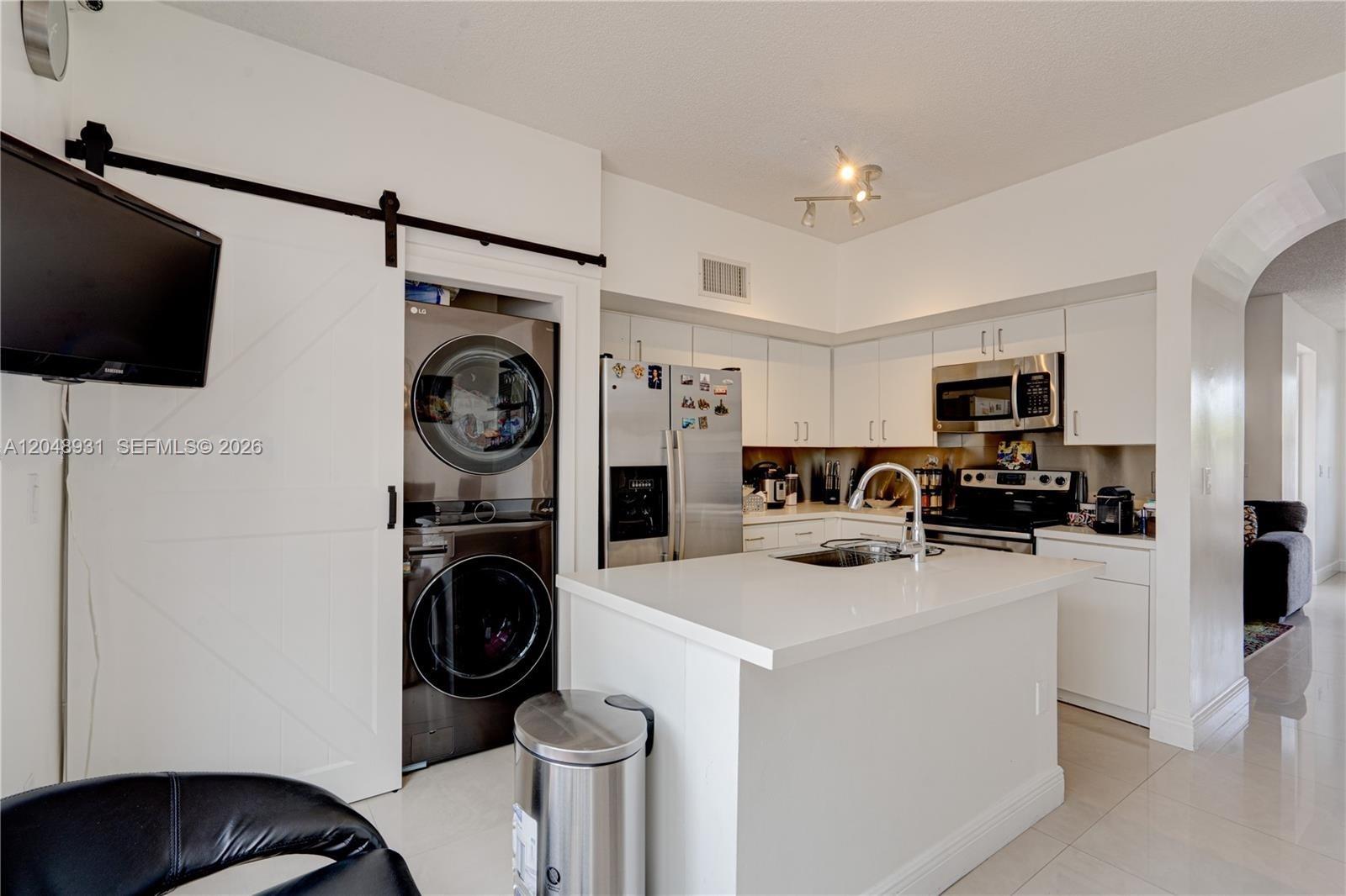 A modern kitchen features white cabinetry, a central island, and a stacked washer and dryer — 8535 SW 152nd Ave # 204, Miami FL 33193, MIAMI, FL