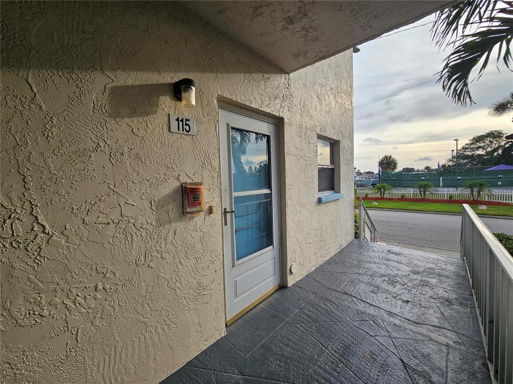 An exterior view of a building entrance with a door labeled 115 and a porch — 2850 59TH STREET S UNIT 115, ST PETERSBURG, FL