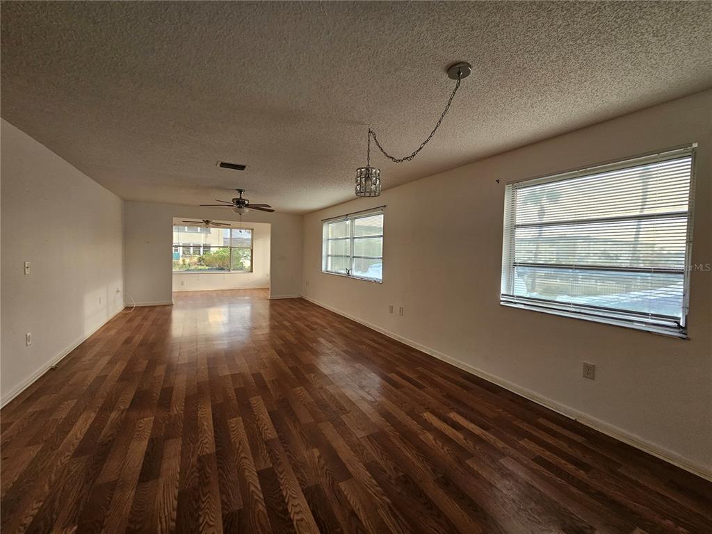 A spacious living room features wood-look flooring, white walls, and two large windows — 2850 59TH STREET S UNIT 115, ST PETERSBURG, FL