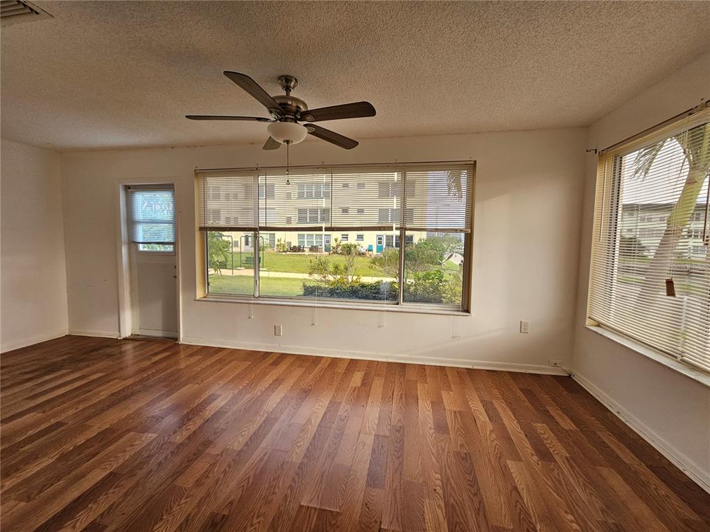 An empty room with wood-look flooring, a ceiling fan, and large windows overlooking a courtyard — 2850 59TH STREET S UNIT 115, ST PETERSBURG, FL