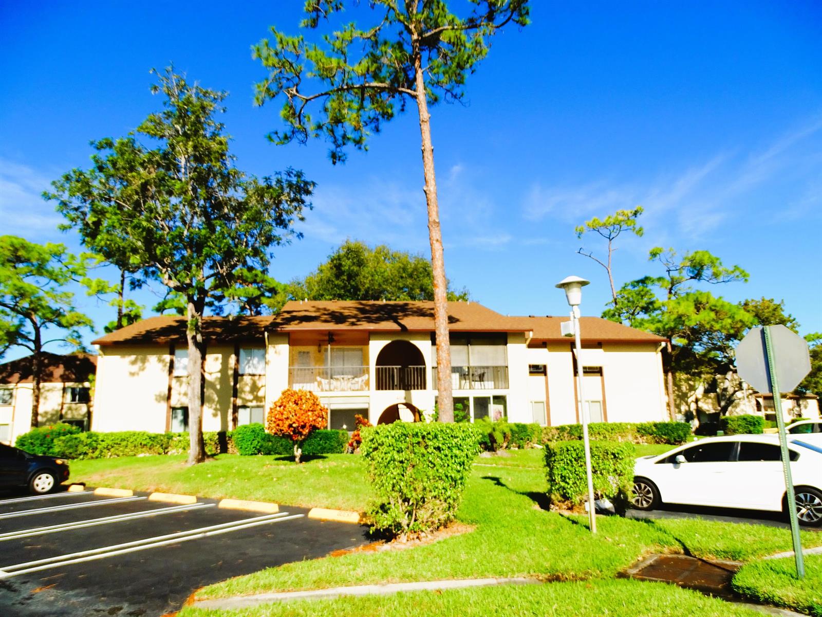 A two-story apartment building with a tan exterior, arched balconies, and surrounding landscaping — 409 Pine Glen Lane # 2, FL 33463, FL