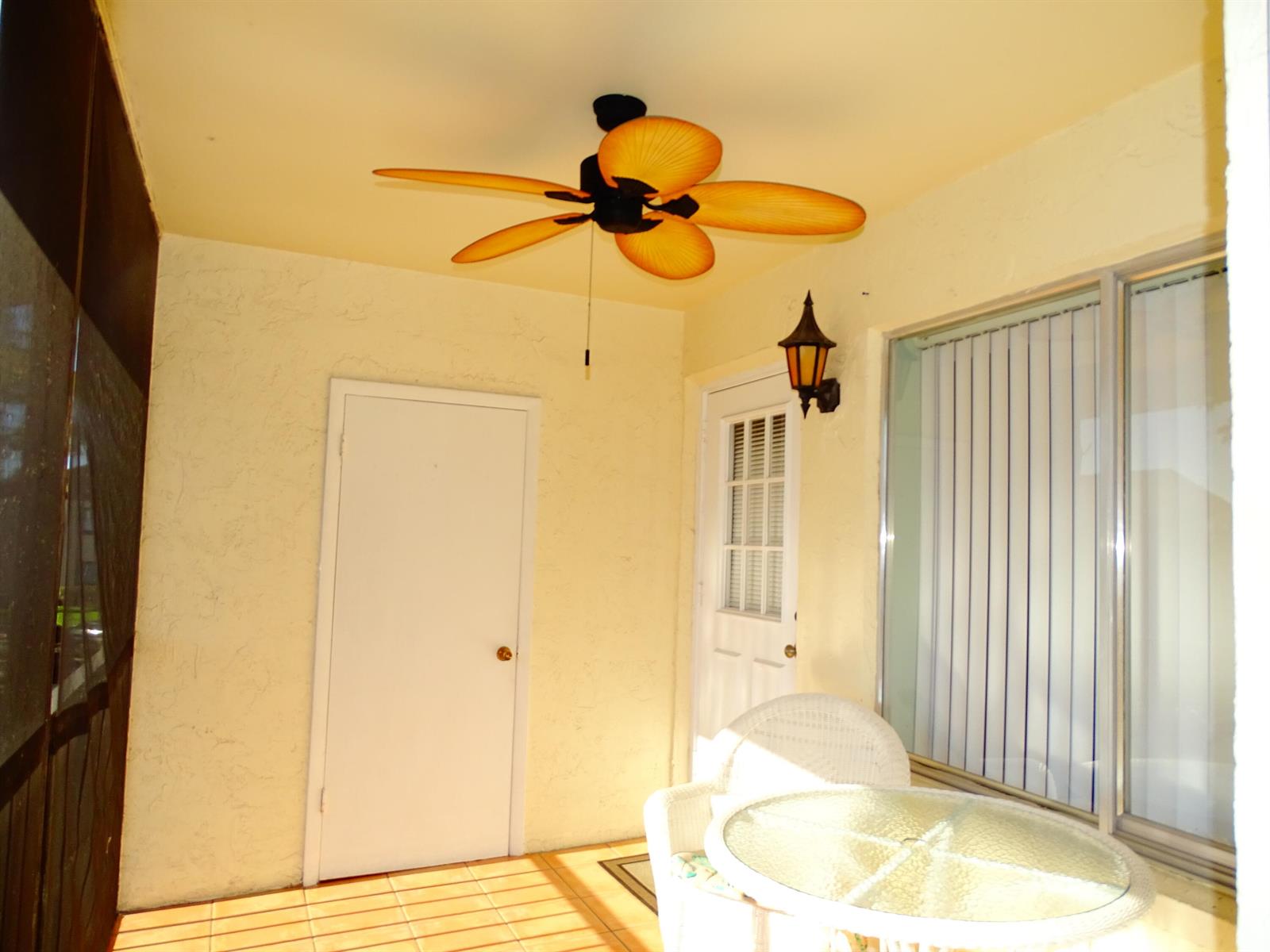 A covered patio features a ceiling fan, a glass table, and two white wicker chairs — 409 Pine Glen Lane # 2, FL 33463, FL