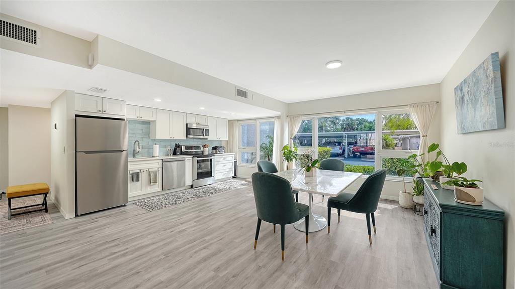 A kitchen and dining area features light wood flooring, white cabinetry, and a marble-topped table — 1100 IMPERIAL DRIVE UNIT 108, SARASOTA, FL