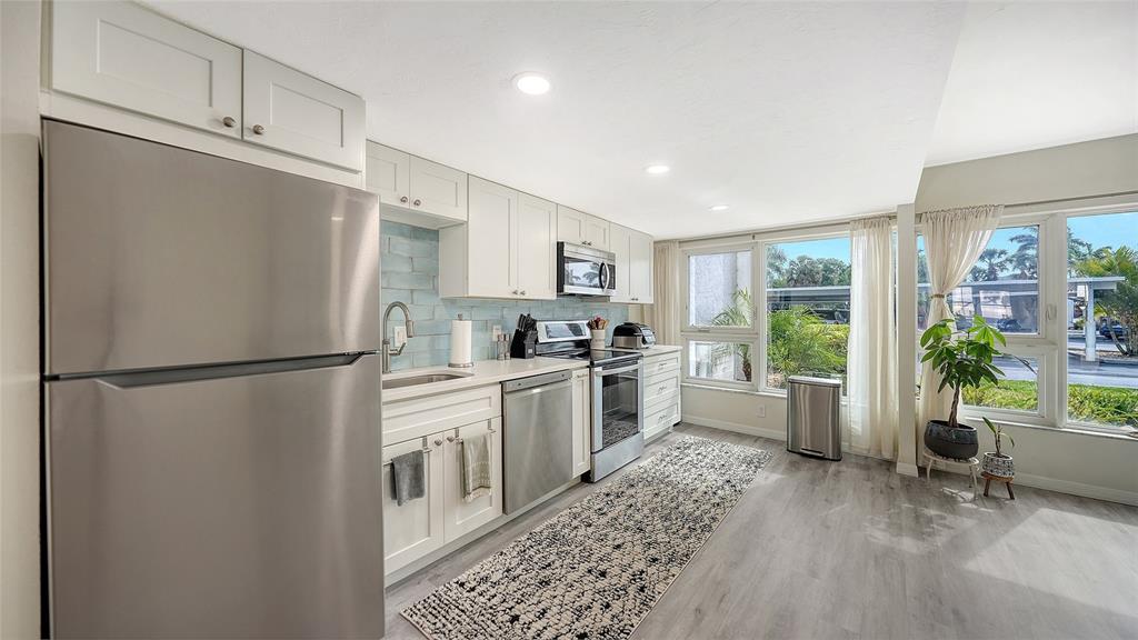A kitchen features white cabinets, stainless steel appliances, a light blue backsplash, and large windows — 1100 IMPERIAL DRIVE UNIT 108, SARASOTA, FL