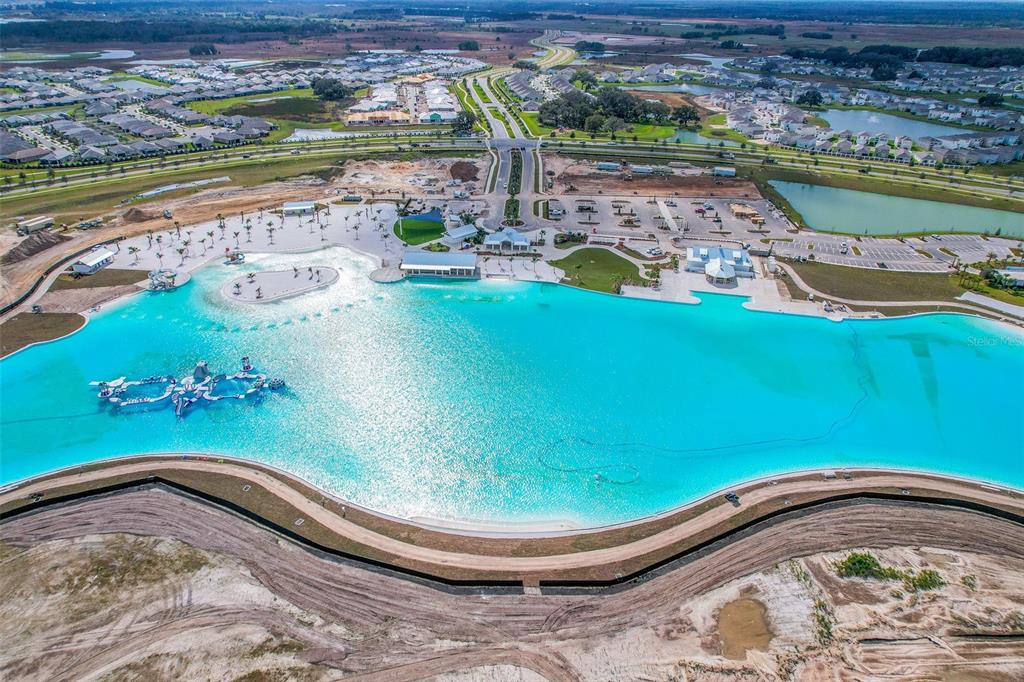 An aerial view shows a large turquoise swimming lagoon with an inflatable obstacle course — 10866 QUAIL GROVE WAY, SAN ANTONIO, FL