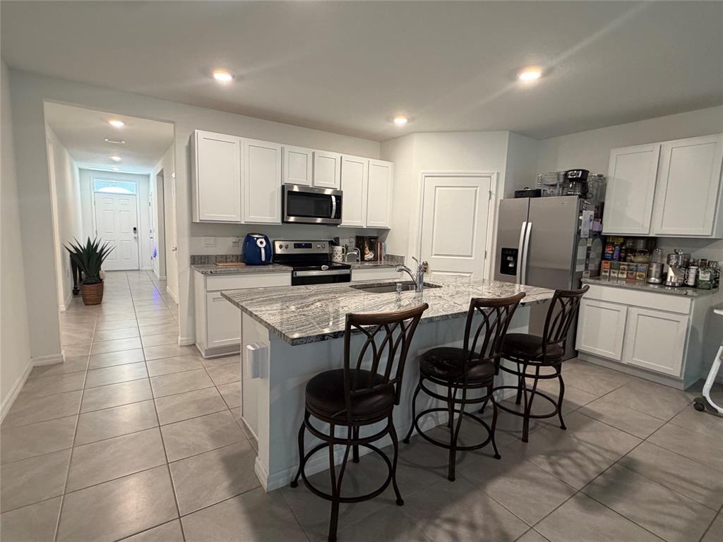 A kitchen features white cabinets, granite countertops, a central island with stools, and tile flooring — 10866 QUAIL GROVE WAY, SAN ANTONIO, FL